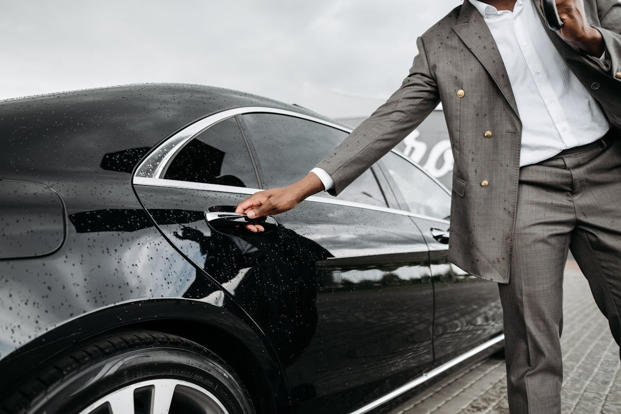 Mastering the First Impression: Your intriguing post title goes here A man in a suit opens a luxury car door under raindrops on stone pavement.